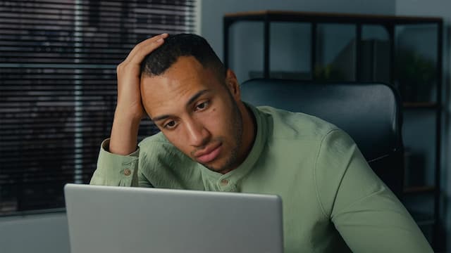 Homem frustrado usando notebook com várias abas abertas durante busca de imóvel online