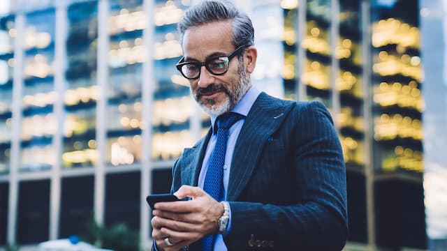 Homem executivo usando celular em área urbana, representando o comportamento do comprador no mercado imobiliário em 2026